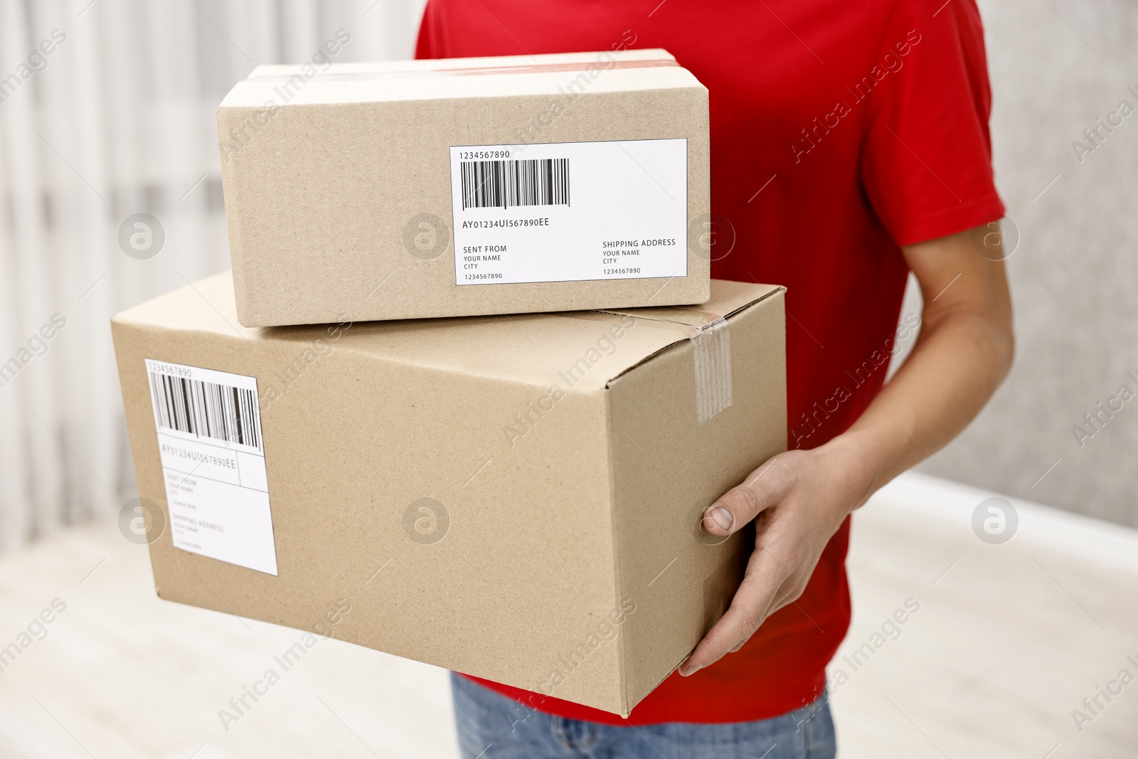 Photo of Man holding parcels with shipping labels indoors, closeup