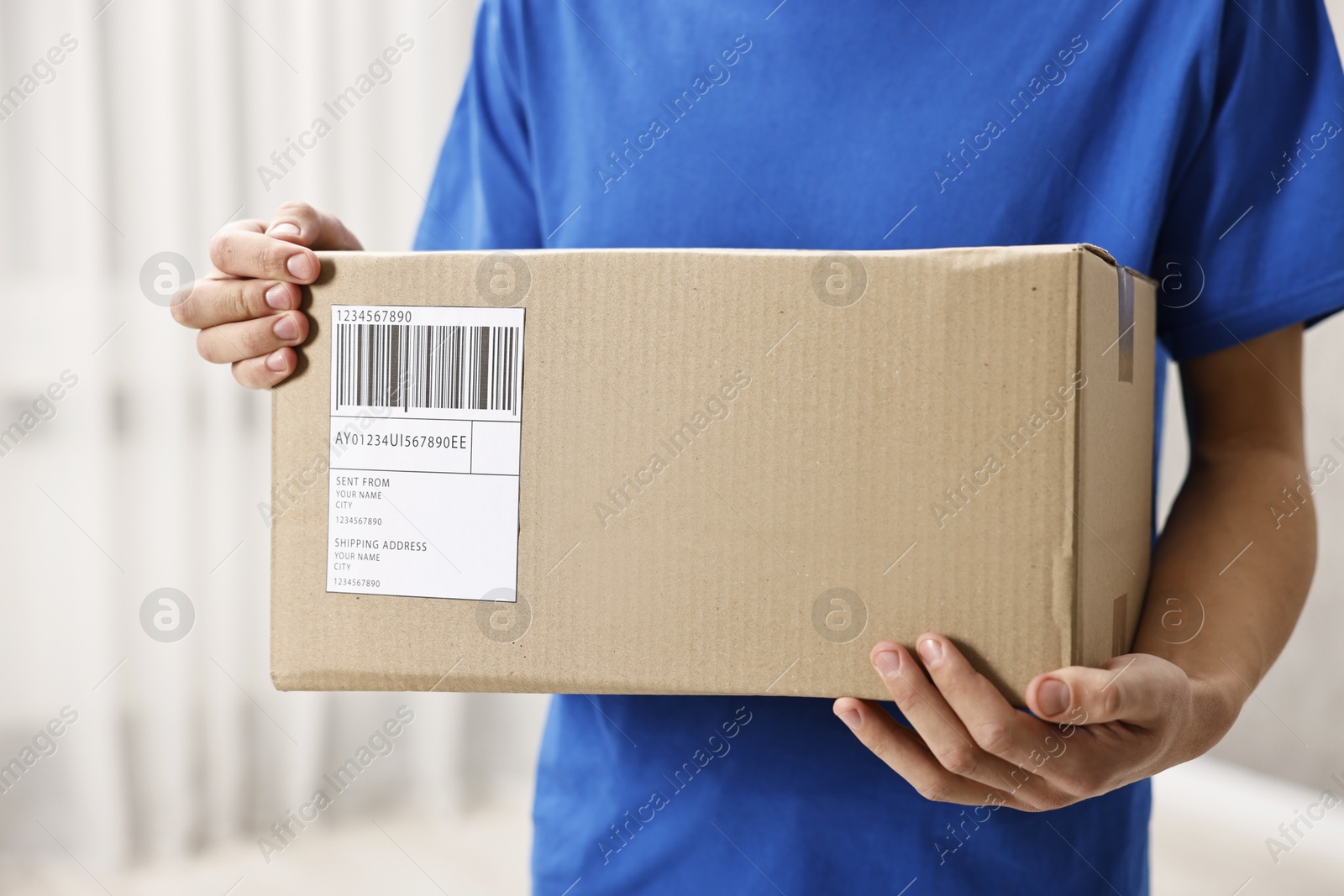 Photo of Man holding parcel with shipping label indoors, closeup