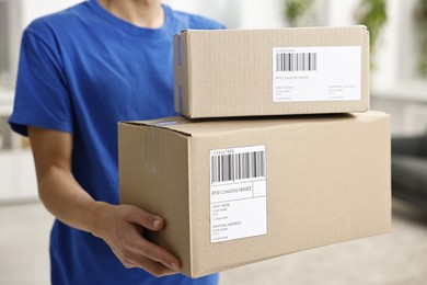 Photo of Man holding parcels with shipping labels indoors, closeup