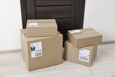 Photo of Cardboard parcel boxes with shipping labels near door indoors