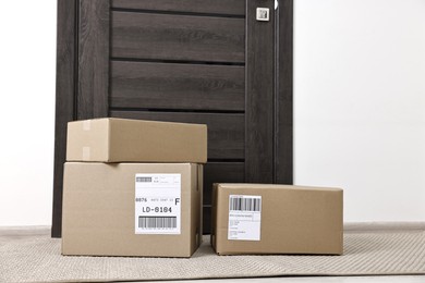 Photo of Cardboard parcel boxes with shipping labels near door indoors