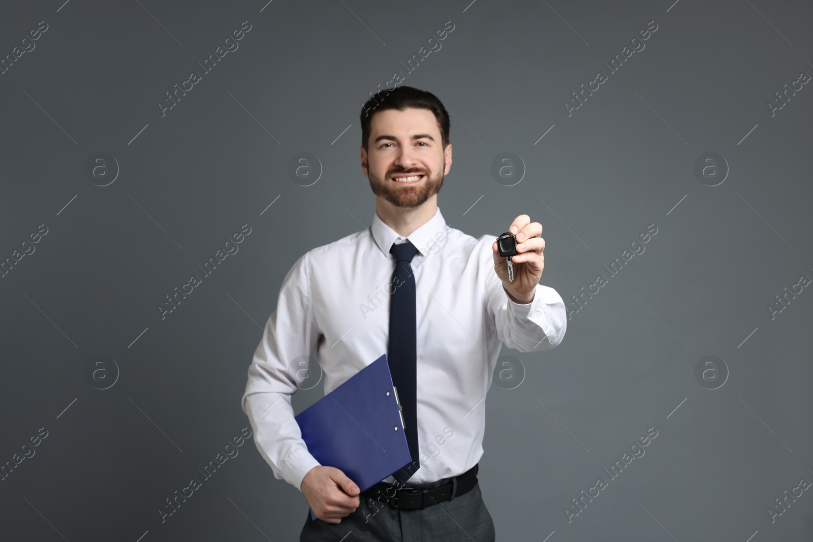 Photo of Cheerful salesman with car key and clipboard on grey background