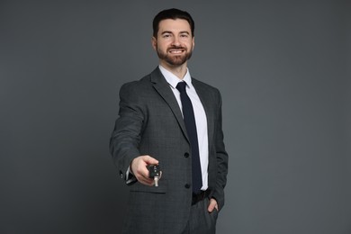 Cheerful salesman with car key on grey background