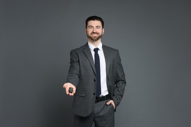 Cheerful salesman with car key on grey background