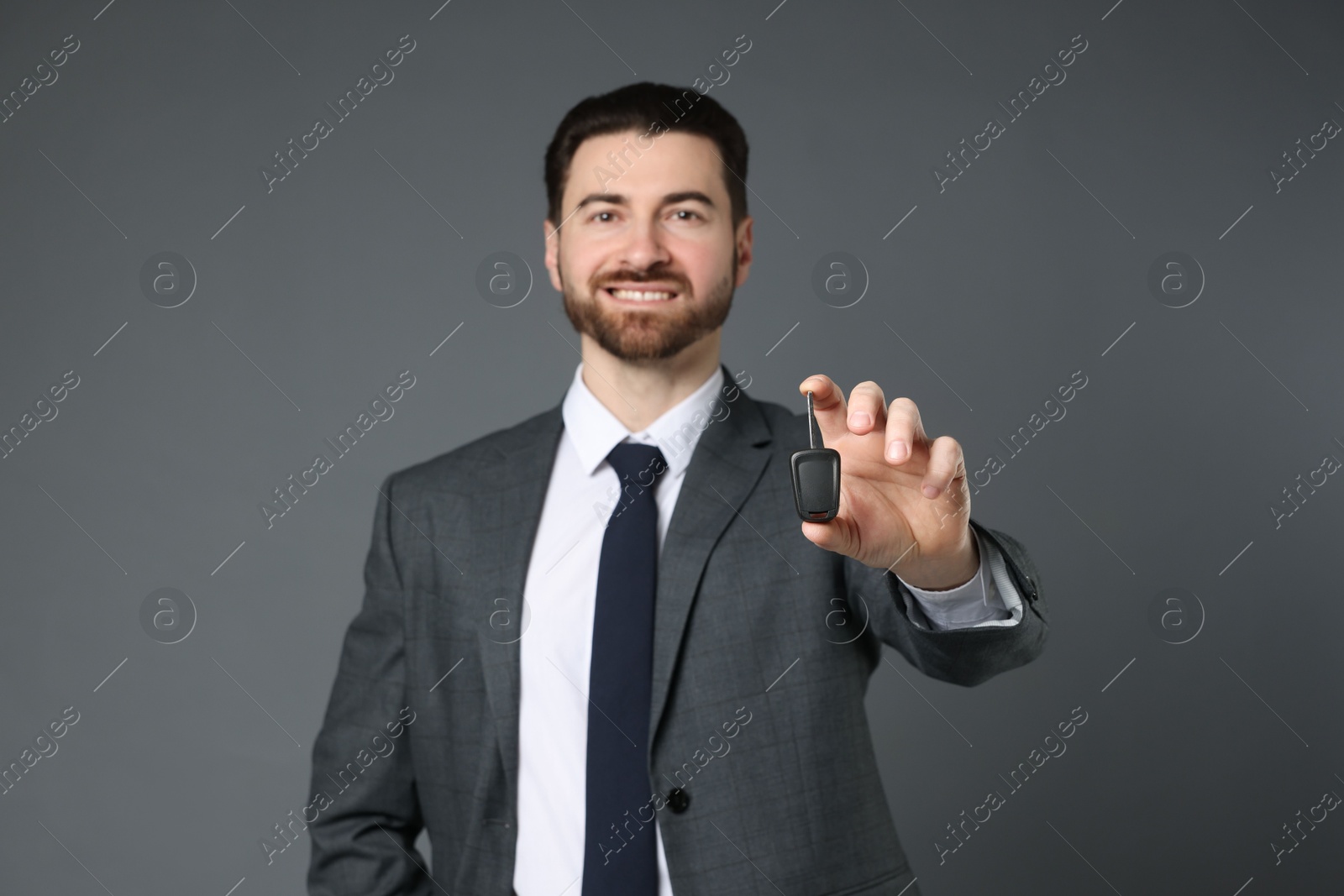 Photo of Cheerful salesman with car key on grey background, selective focus