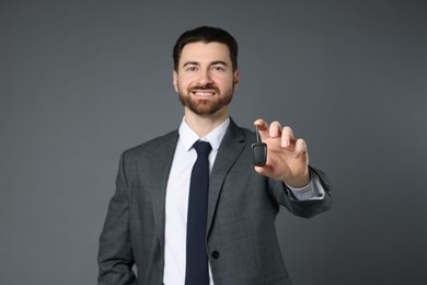 Photo of Cheerful salesman with car key on grey background, selective focus