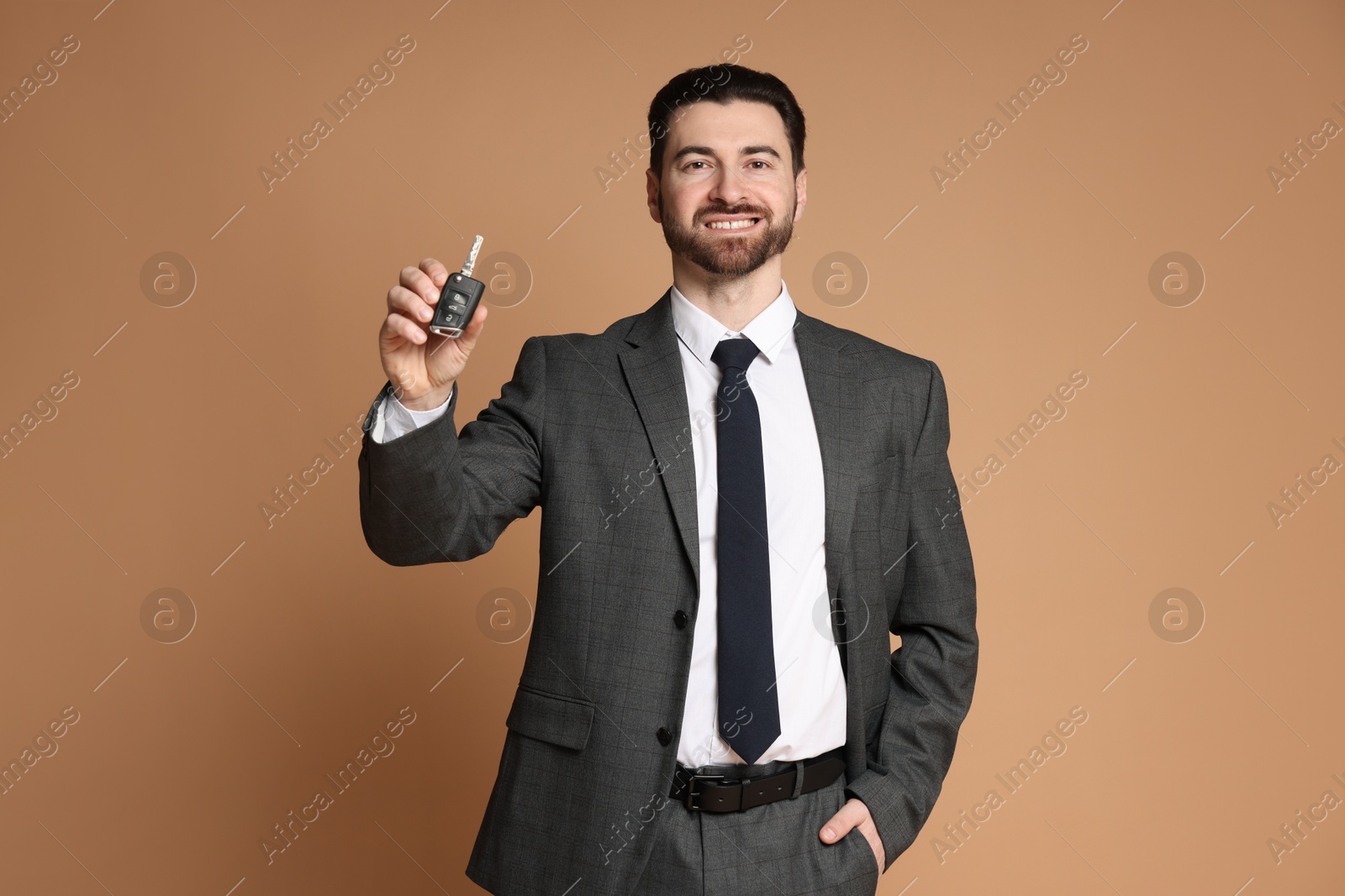 Photo of Cheerful salesman with car key on beige background