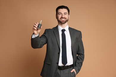 Cheerful salesman with car key on beige background