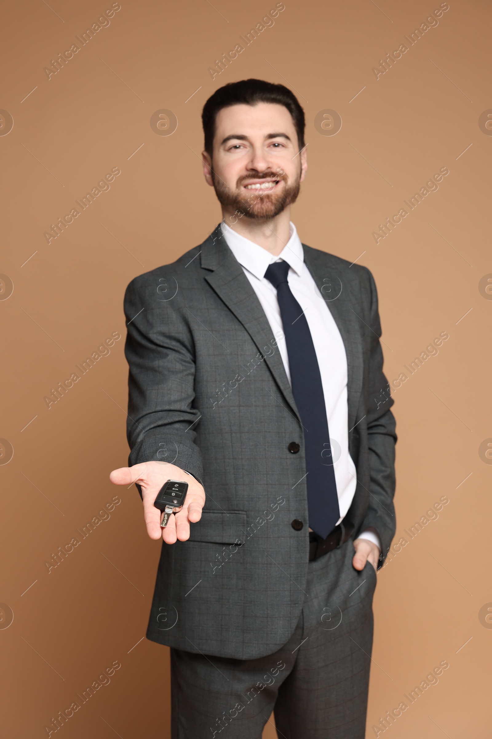 Photo of Cheerful salesman with car key on beige background