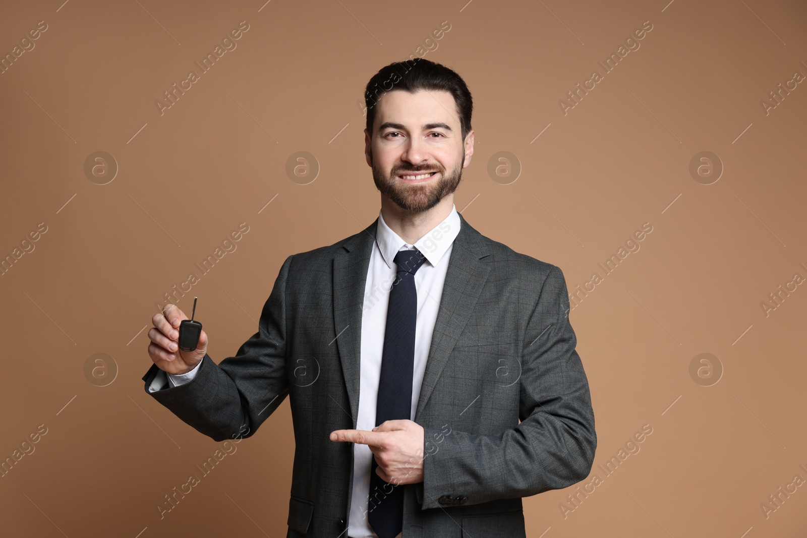 Photo of Cheerful salesman pointing at car key on beige background