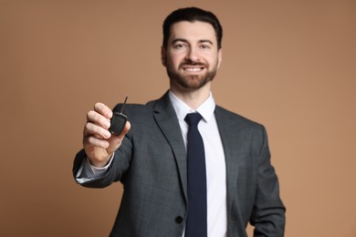 Photo of Cheerful salesman with car key on beige background, selective focus