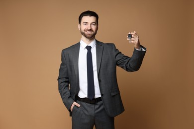 Cheerful salesman with car key on beige background