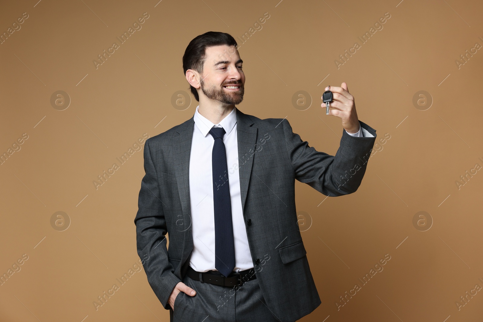 Photo of Cheerful salesman with car key on beige background