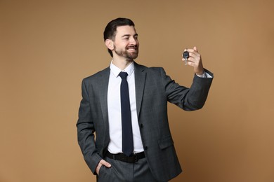 Cheerful salesman with car key on beige background