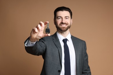 Photo of Cheerful salesman with car key on beige background, selective focus