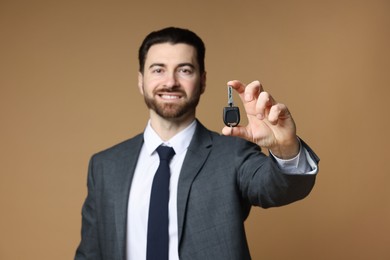 Cheerful salesman with car key on beige background, selective focus