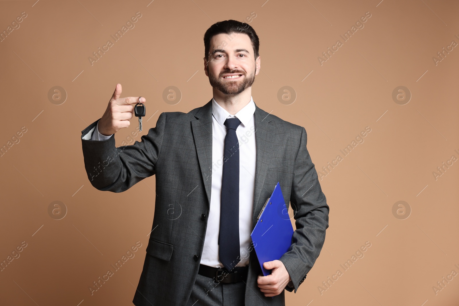 Photo of Cheerful salesman with car key and clipboard on beige background