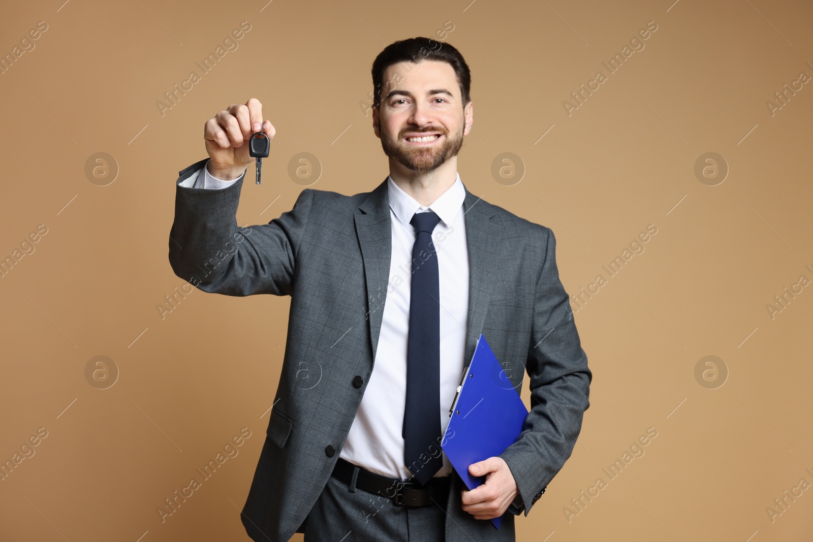 Photo of Cheerful salesman with car key and clipboard on beige background