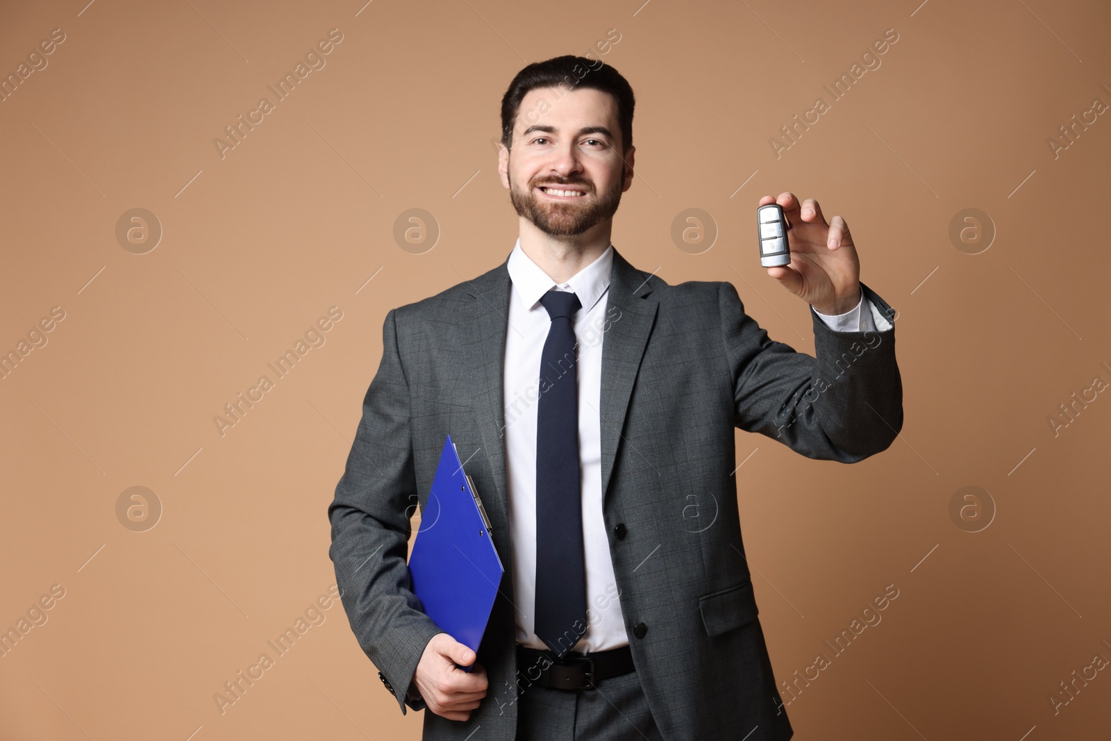 Photo of Cheerful salesman with car key and clipboard on beige background