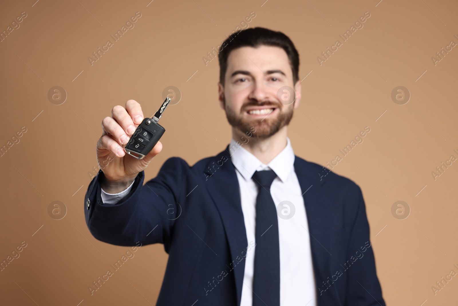 Photo of Cheerful salesman with car key on beige background, selective focus