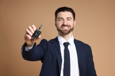 Cheerful salesman with car key on beige background, selective focus