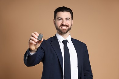 Cheerful salesman with car key on beige background