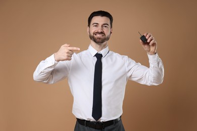 Cheerful salesman pointing at car key on beige background