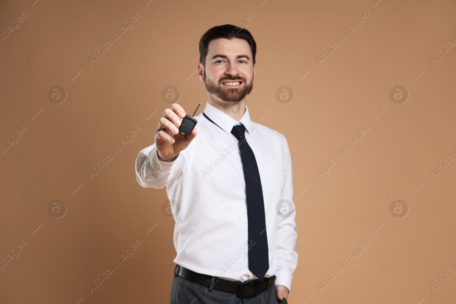 Photo of Cheerful salesman with car key on beige background