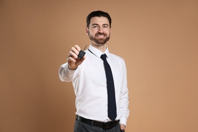 Photo of Cheerful salesman with car key on beige background