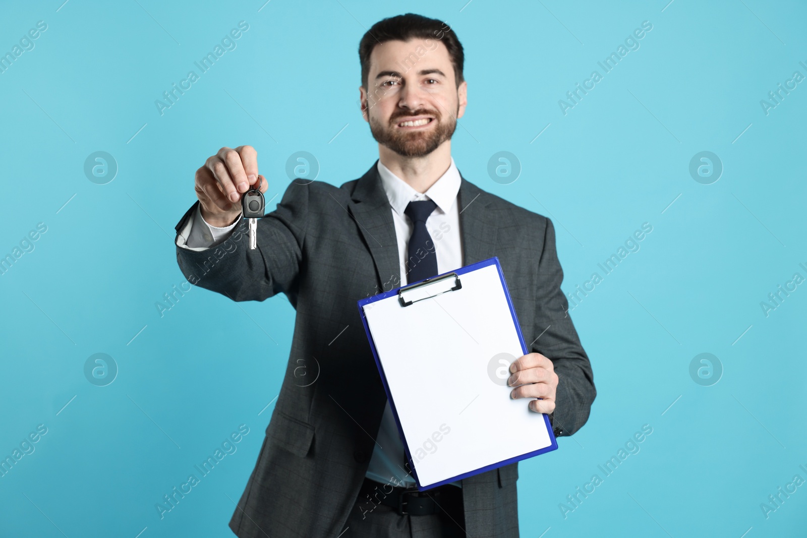 Photo of Cheerful salesman with car key and clipboard on light blue background