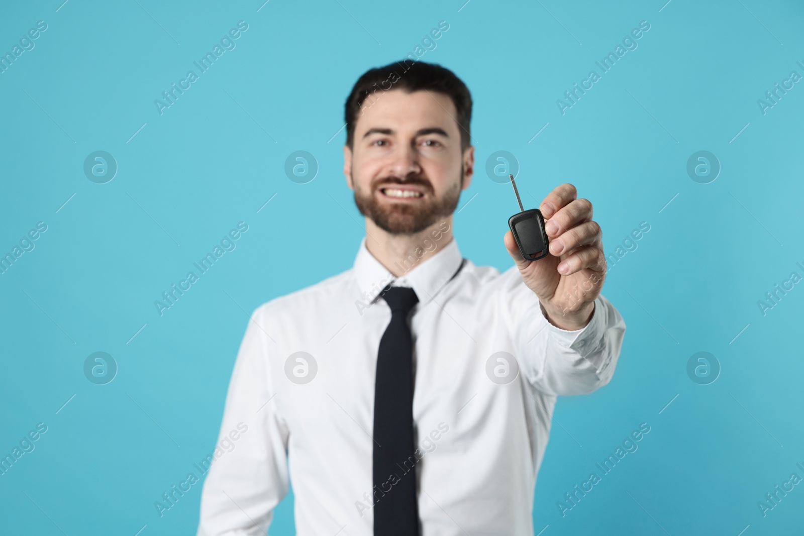 Photo of Cheerful salesman with car key on light blue background, selective focus