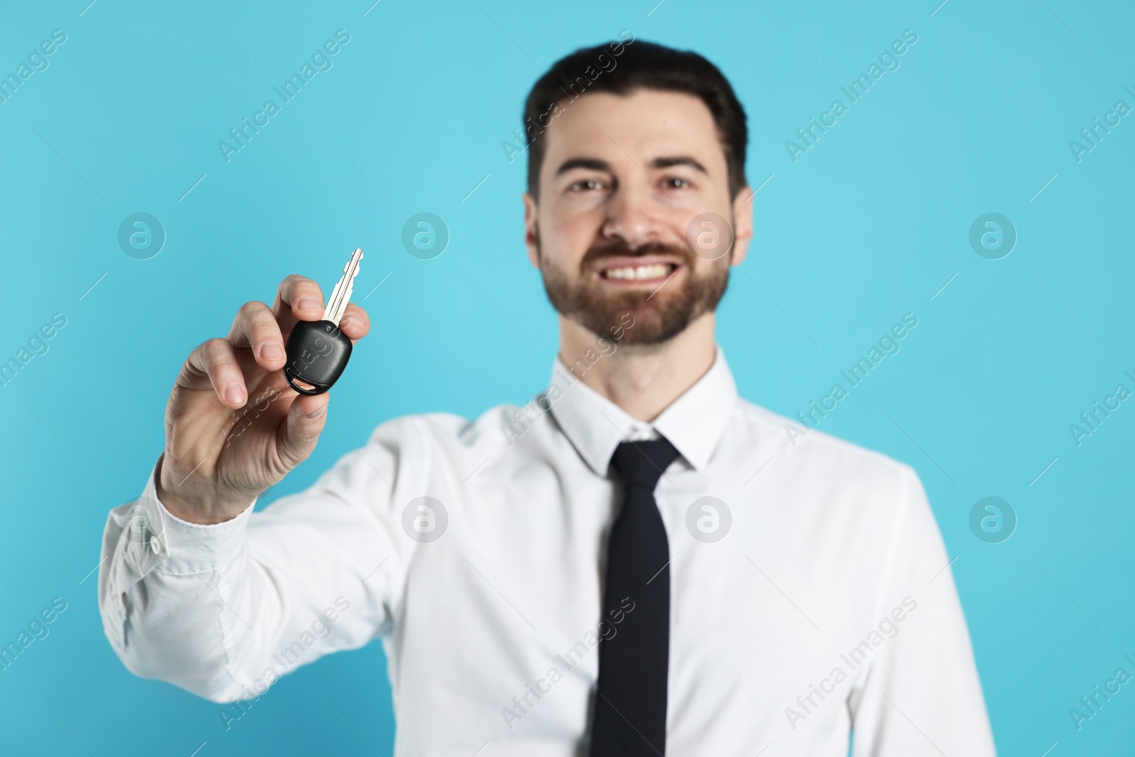 Photo of Cheerful salesman with car key on light blue background, selective focus