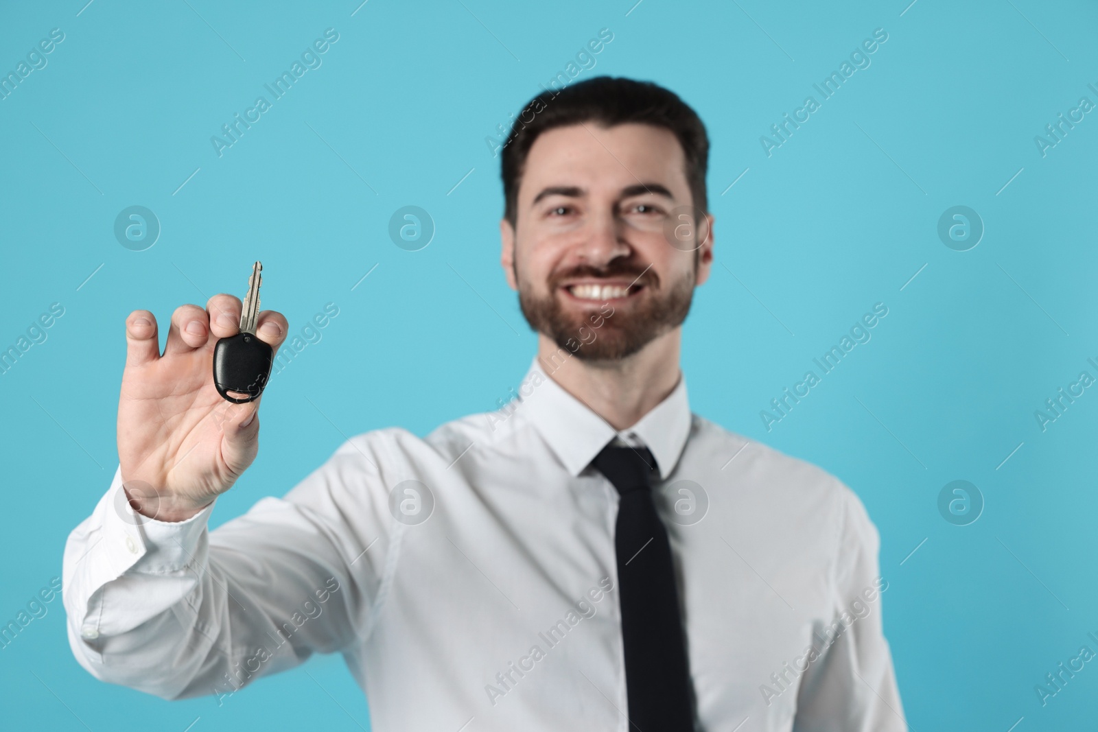 Photo of Cheerful salesman with car key on light blue background, selective focus