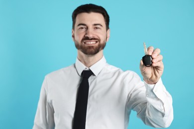 Photo of Cheerful salesman with car key on light blue background, selective focus