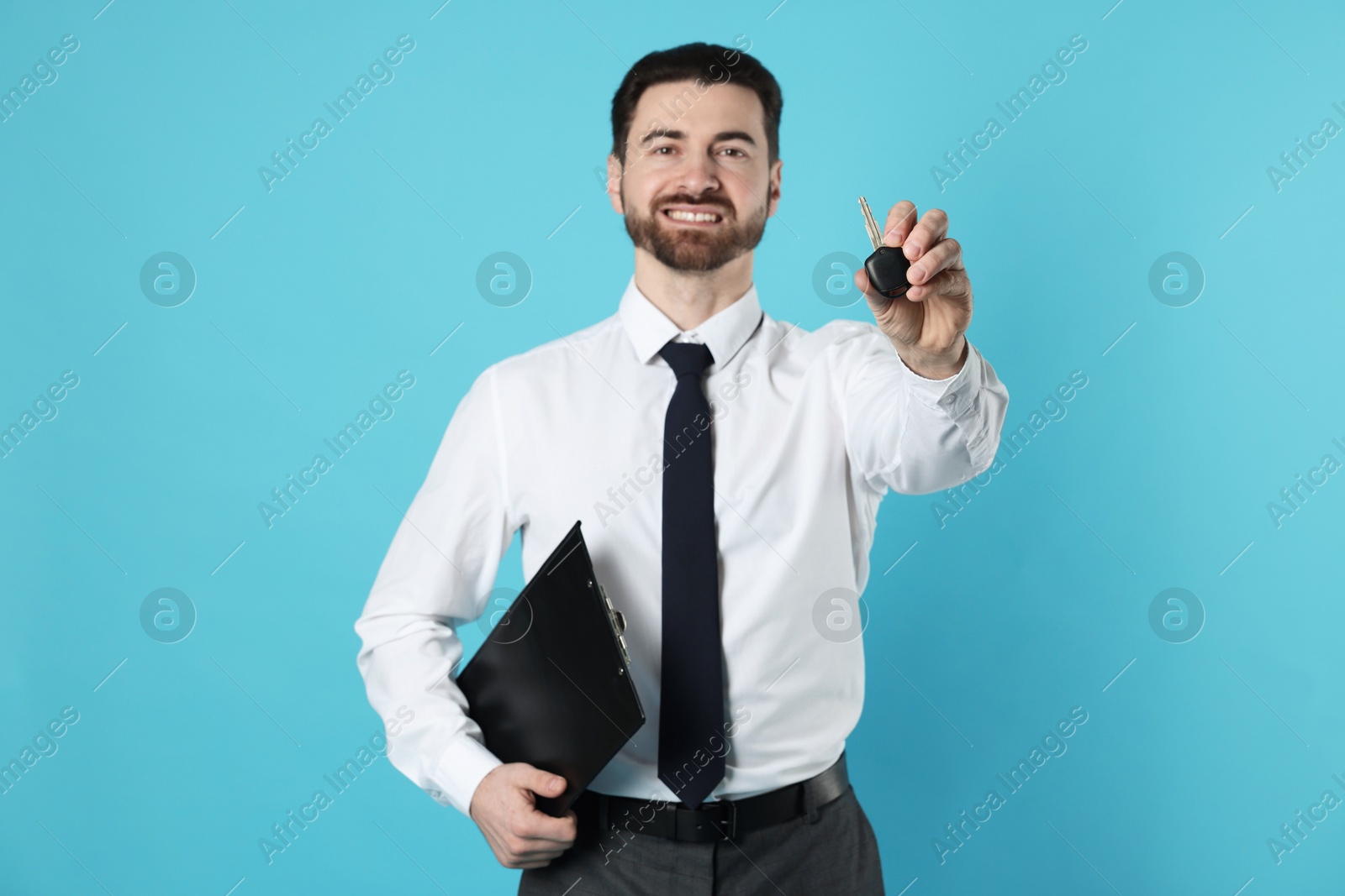 Photo of Cheerful salesman with car key and clipboard on light blue background, selective focus