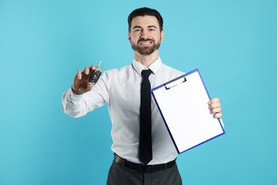 Cheerful salesman with car key and clipboard on light blue background