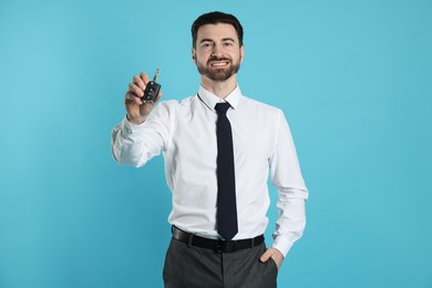 Cheerful salesman with car key on light blue background