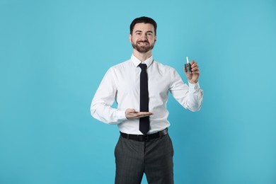 Photo of Cheerful salesman with car key on light blue background