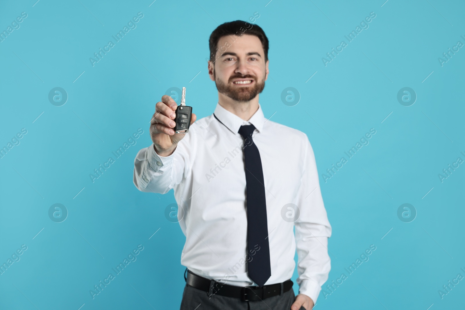 Photo of Cheerful salesman with car key on light blue background