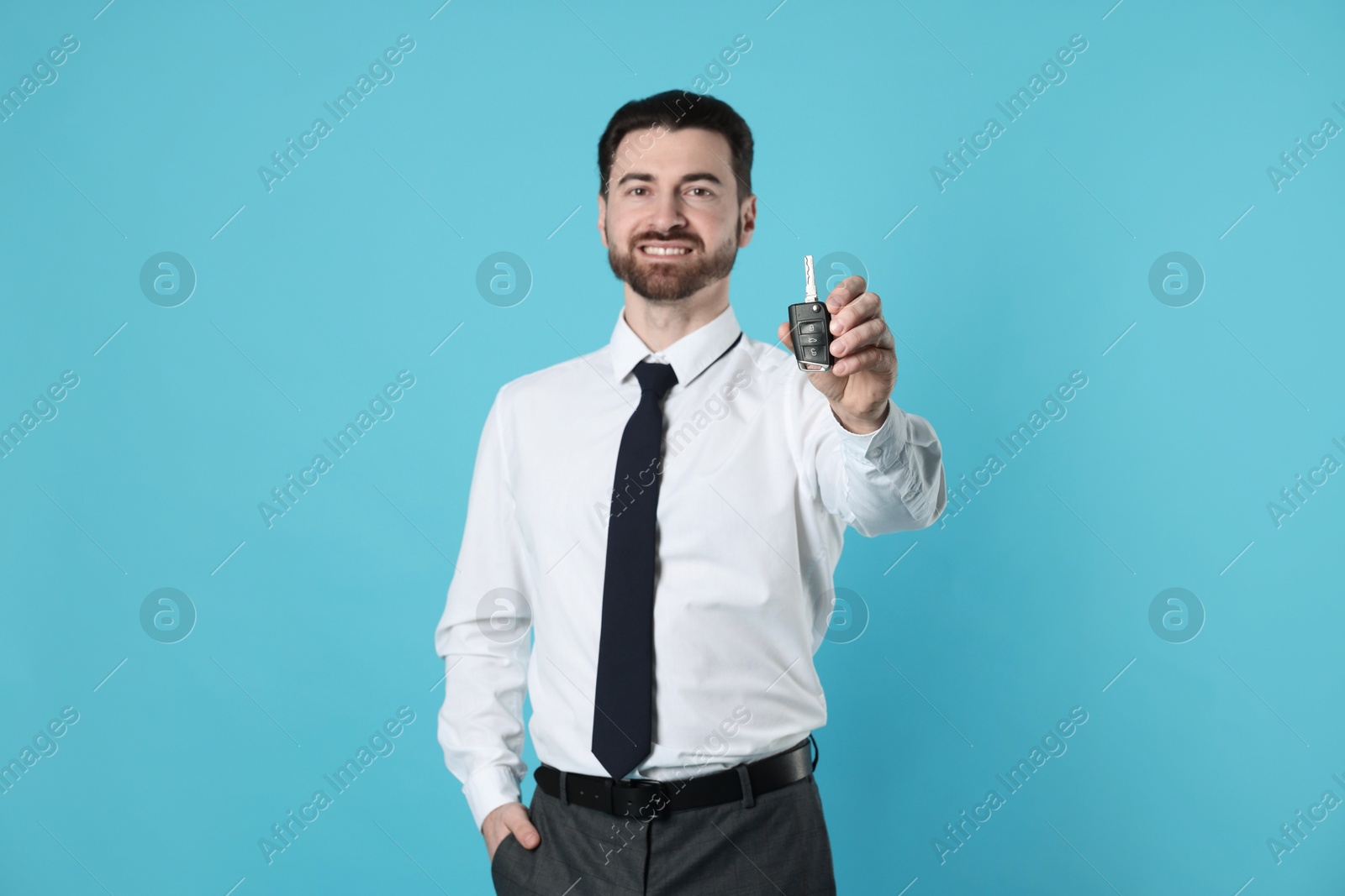 Photo of Cheerful salesman with car key on light blue background