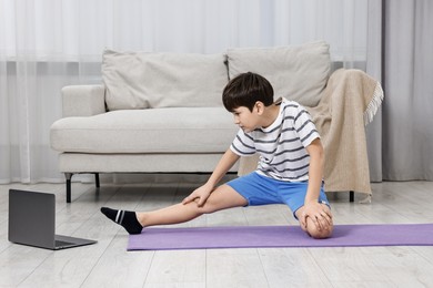 Photo of Little boy exercising near laptop at home. Morning routine