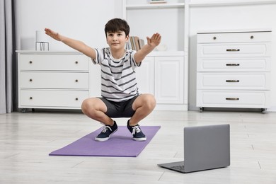 Little boy exercising near laptop at home. Morning routine