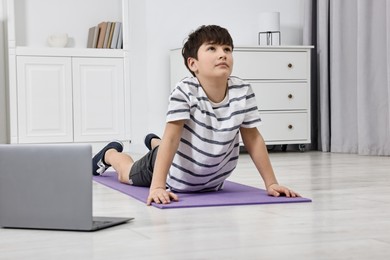 Photo of Little boy exercising near laptop at home. Morning routine