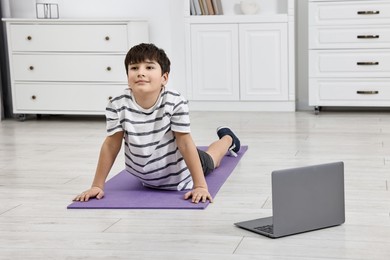 Photo of Little boy exercising near laptop at home. Morning routine