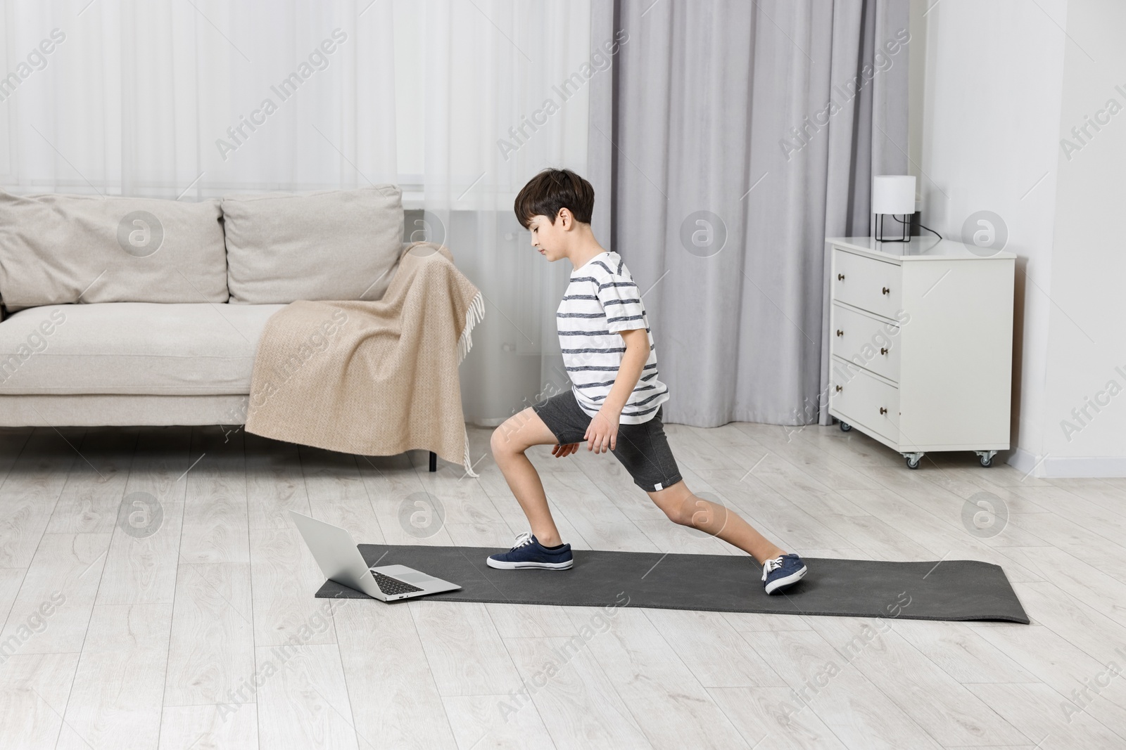 Photo of Little boy exercising near laptop at home. Morning routine