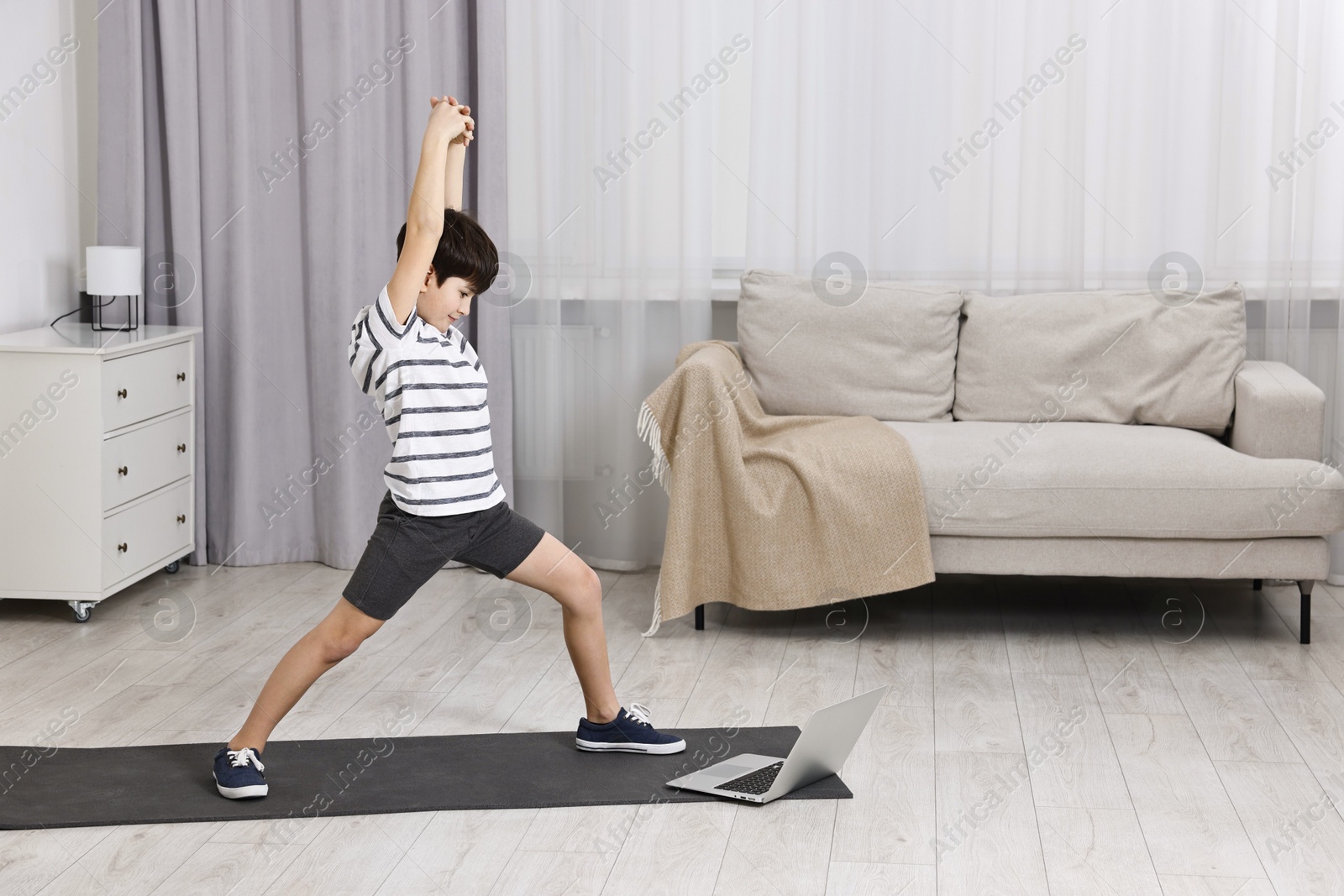 Photo of Little boy exercising near laptop at home. Morning routine