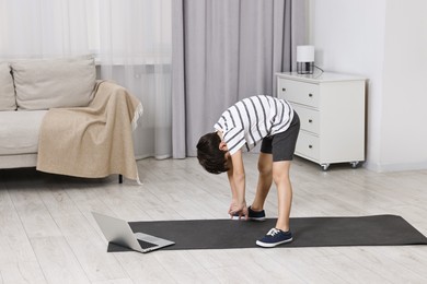 Photo of Little boy exercising near laptop at home. Morning routine