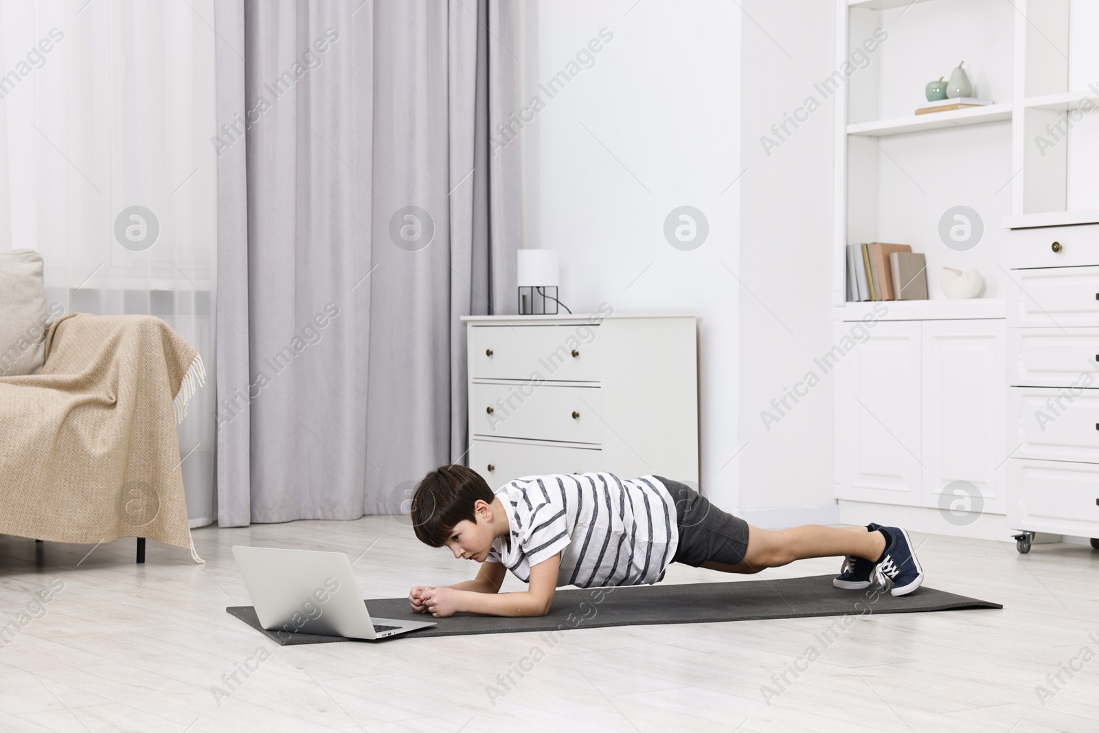 Photo of Little boy doing plank exercise near laptop at home. Morning routine