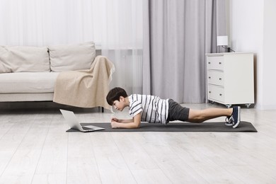 Photo of Little boy doing plank exercise near laptop at home. Morning routine