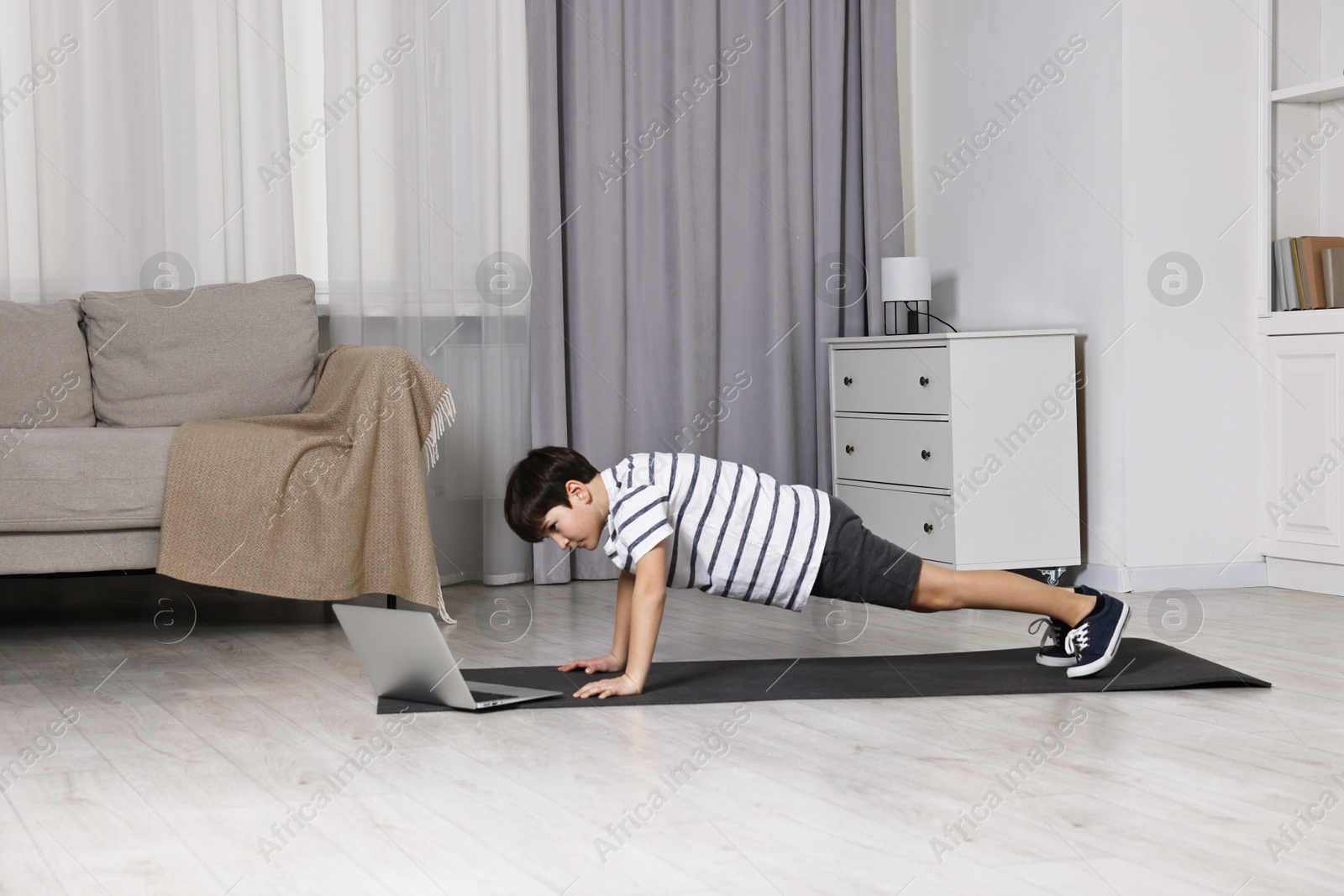 Photo of Little boy exercising near laptop at home. Morning routine